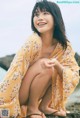 A woman in a yellow kimono sitting on the beach.