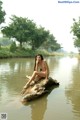 A naked woman sitting on a log in the water.