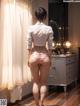 A woman in a white shirt and pink panties standing in front of a mirror.