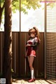 A girl in a red and white uniform standing next to a fence.