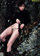 A woman in a black turtle neck sweater and thigh high boots posing on a rock.